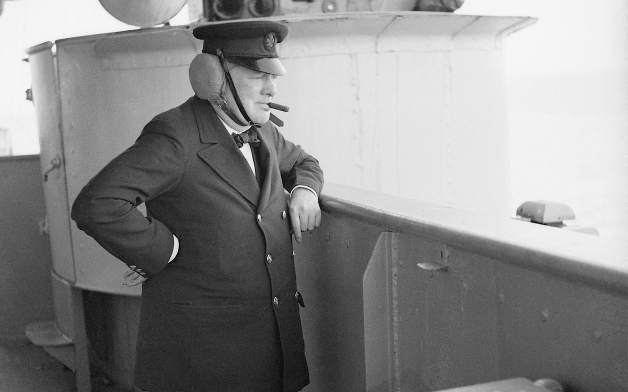 Winston Churchill, with leather ear guards, watching gunnery practice on HMS Renown